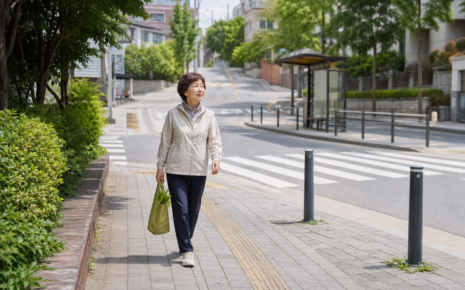 동네 보행로에서 약국과 버스 정류장 방향을 살피며 걷는 60대 한국인 여성