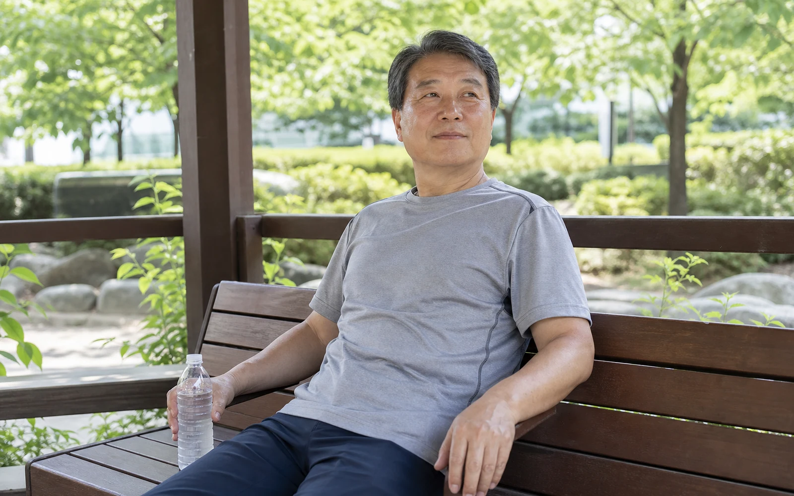 여름 공원 그늘 벤치에 안전하게 앉아 물을 곁에 두고 쉬는 60대 남성